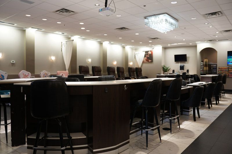 Nail salon interior with dark chairs, white countertops, and overhead lighting.