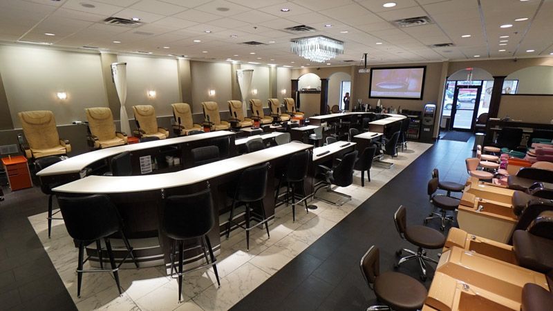 Nail salon interior with manicure stations, client seating, and a bar-style area with stools.