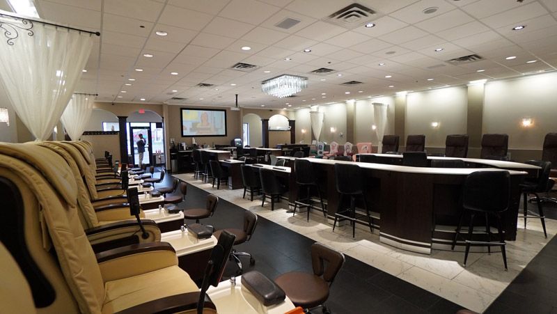 Nail salon interior with rows of tan chairs and a central service area with black stools.