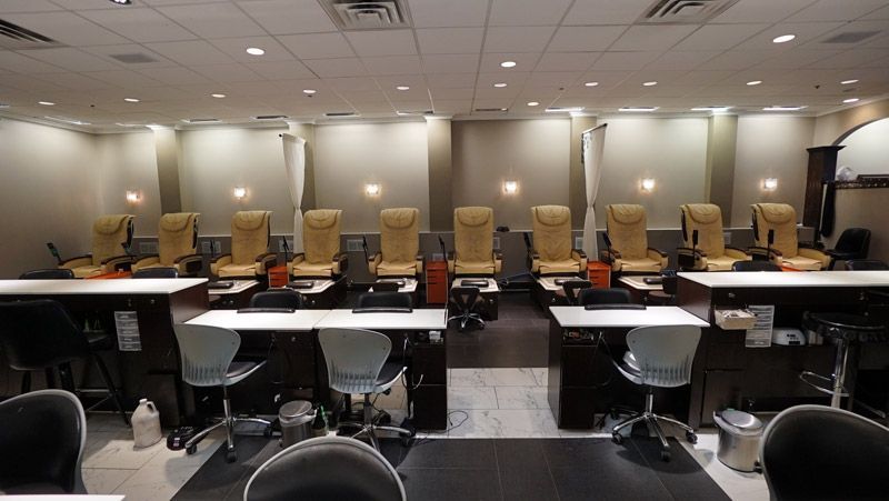 Nail salon interior with rows of tan chairs, white tables, and black chairs, ready for customers.