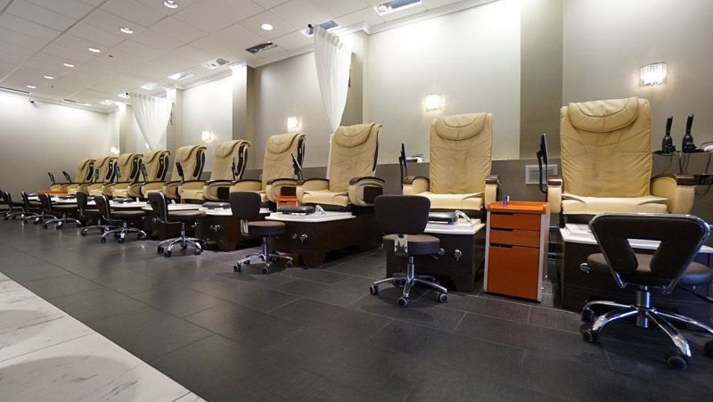 Interior of a nail salon with several beige pedicure chairs and black technician chairs in a row.