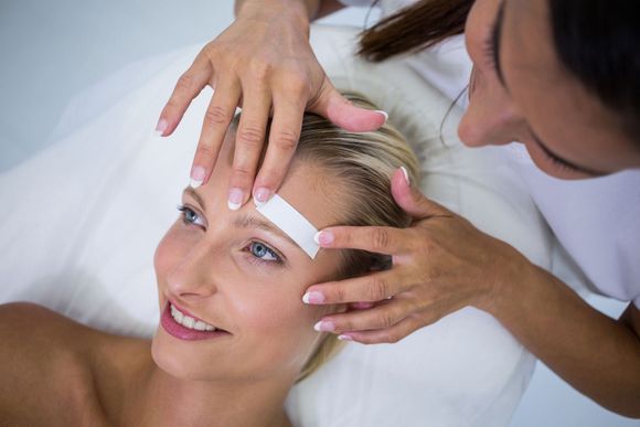 Woman having her upper lip waxed, blue-gloved hands holding a waxing strip.