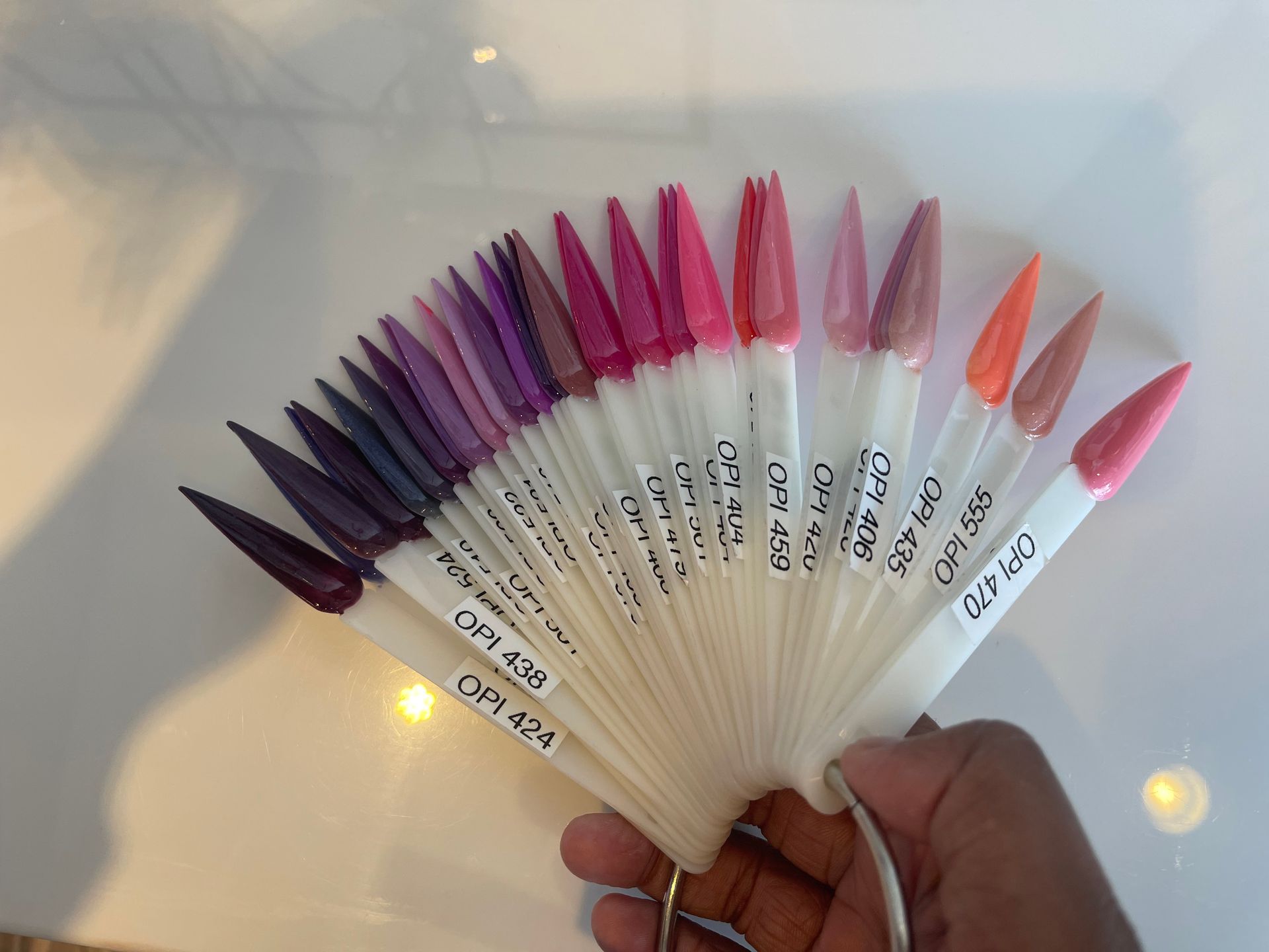 A hand holding a fan of nail polish swatches in various shades of pink, purple, and orange.