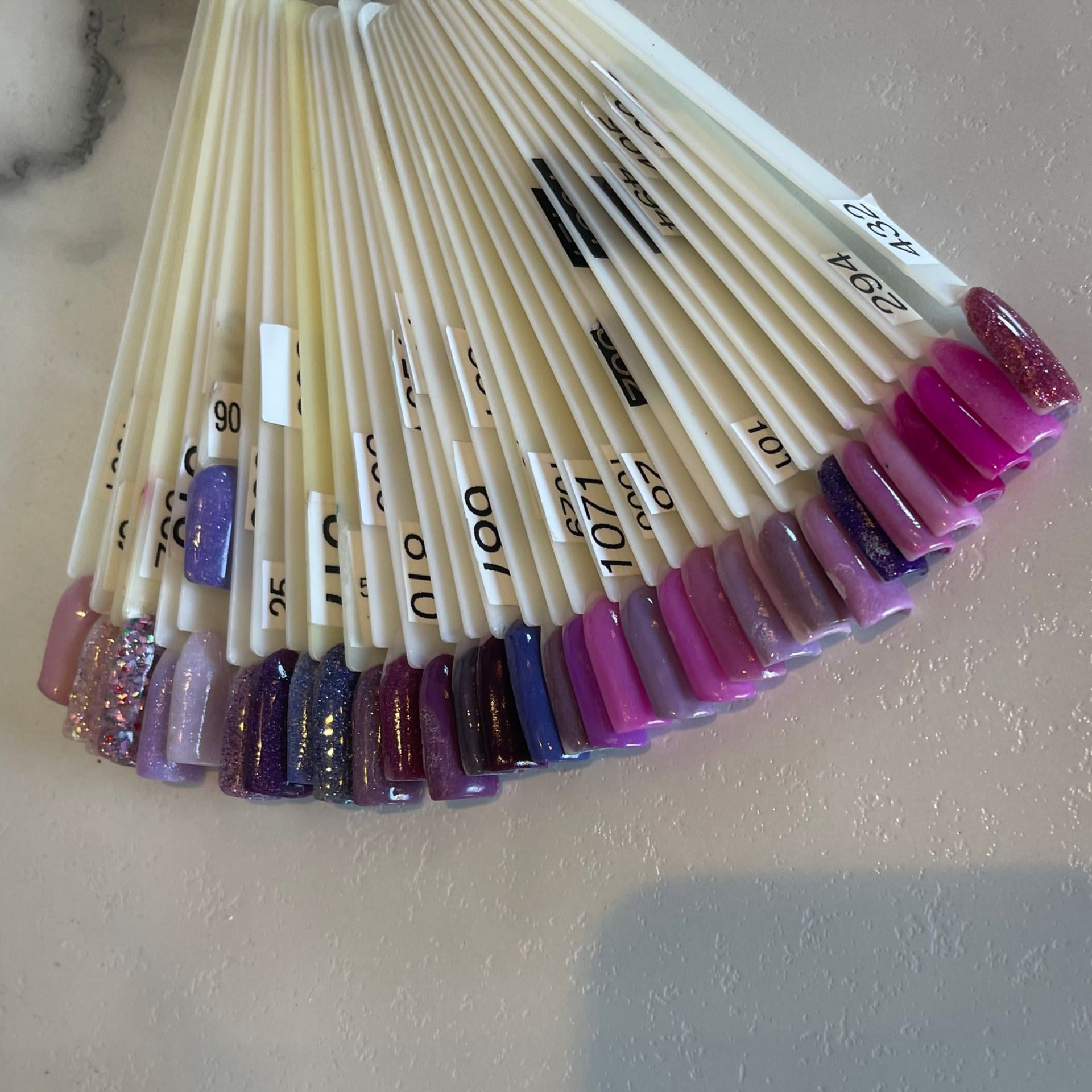 Nail polish color swatches arranged on a fan, shades of purple and pink.