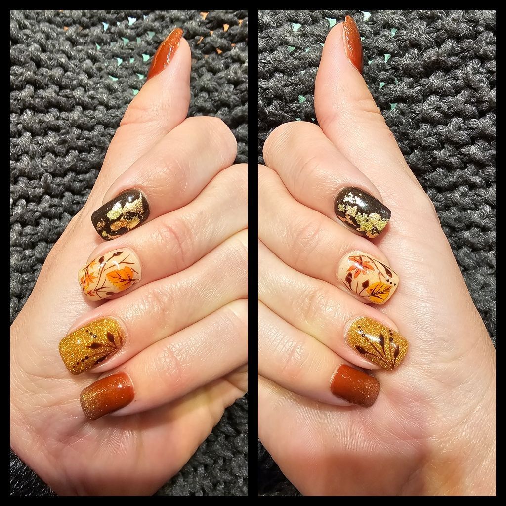 Two hands with fall-themed nail art: brown, gold, and orange colors with leaf and metallic accents.