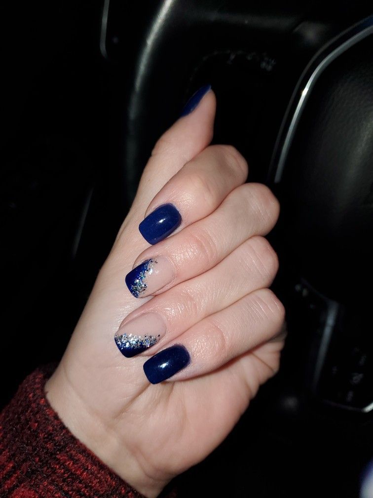 Hand with dark blue nails, one with silver glitter. Inside a car, dark setting.
