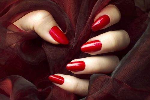 Hand with red nail polish against a burgundy fabric backdrop.