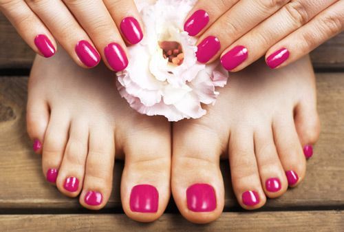 Hands and feet with matching pink nail polish, resting on a wooden surface, with a white flower.