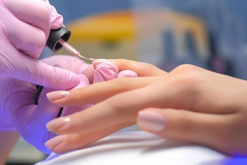 Person receiving a manicure. A gloved hand paints the nails of another. Light pink polish being applied.