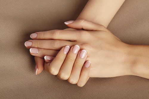 Hands with French manicured nails, resting on a beige surface.