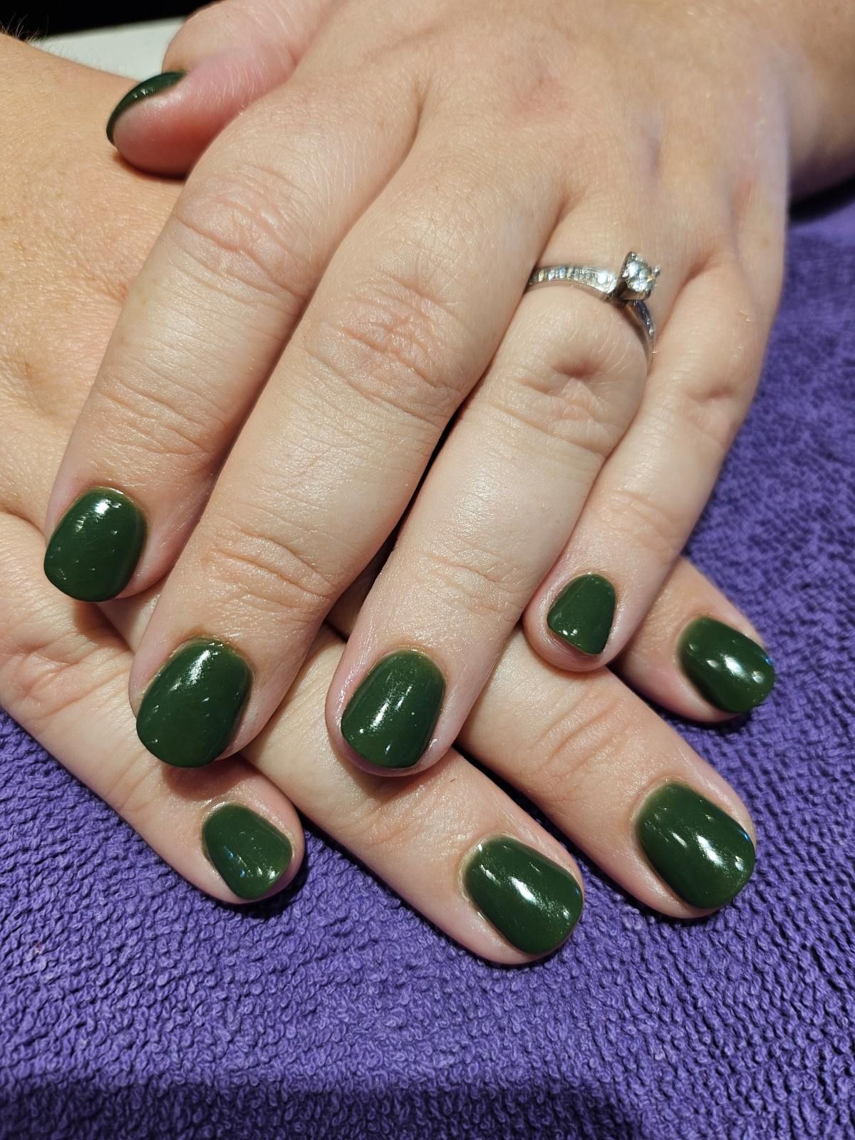 Hands with short, dark green nails resting on a purple towel. A ring is visible on one finger.