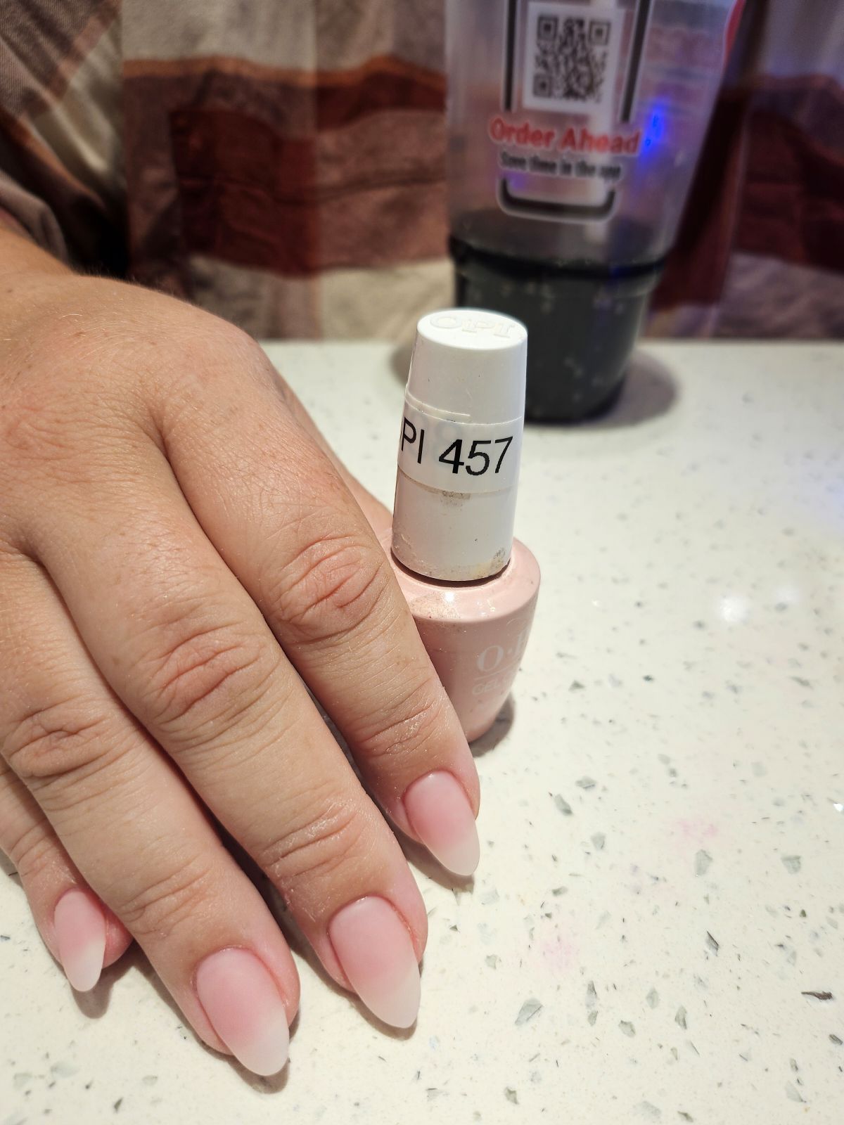 Hand holding a nail polish bottle (OPI 457) next to neatly manicured nails with a pink ombre effect.