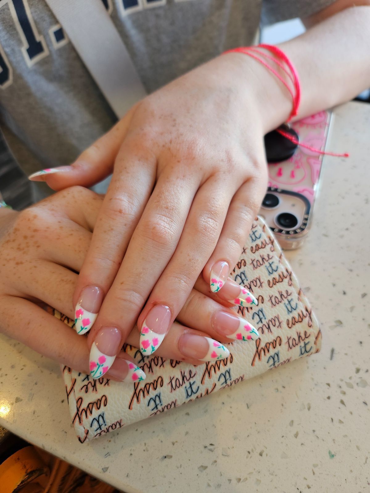 Person's hands with long, pink and white floral designed nails. They are resting on a case with 