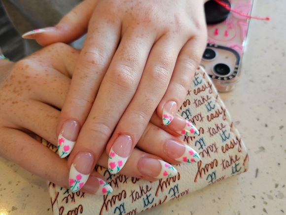 Hands with blue nails and white accent nails, resting on a white towel near nail polish and perfume.