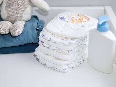 Una pila di pannolini posta sopra un fasciatoio accanto a una bottiglia di shampoo.
