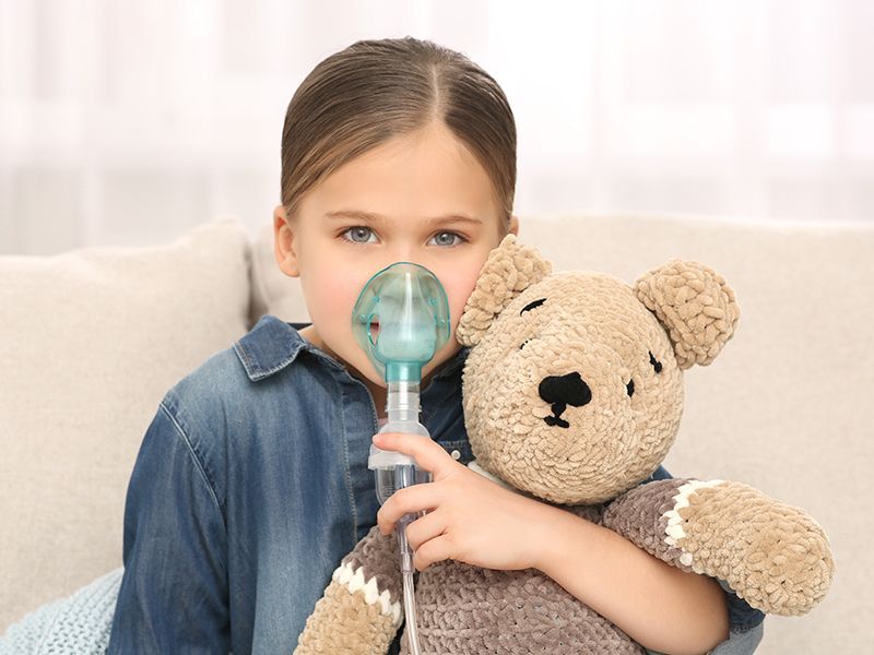 Una bambina tiene in mano un orsacchiotto e usa un inalatore.