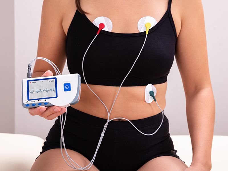 Una donna è seduta su un letto con un cardiofrequenzimetro attaccato al petto.