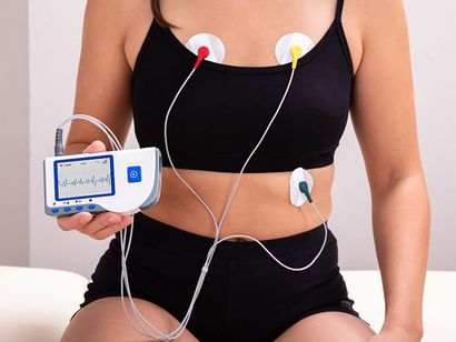 Una donna è seduta su un letto con un cardiofrequenzimetro attaccato al petto.
