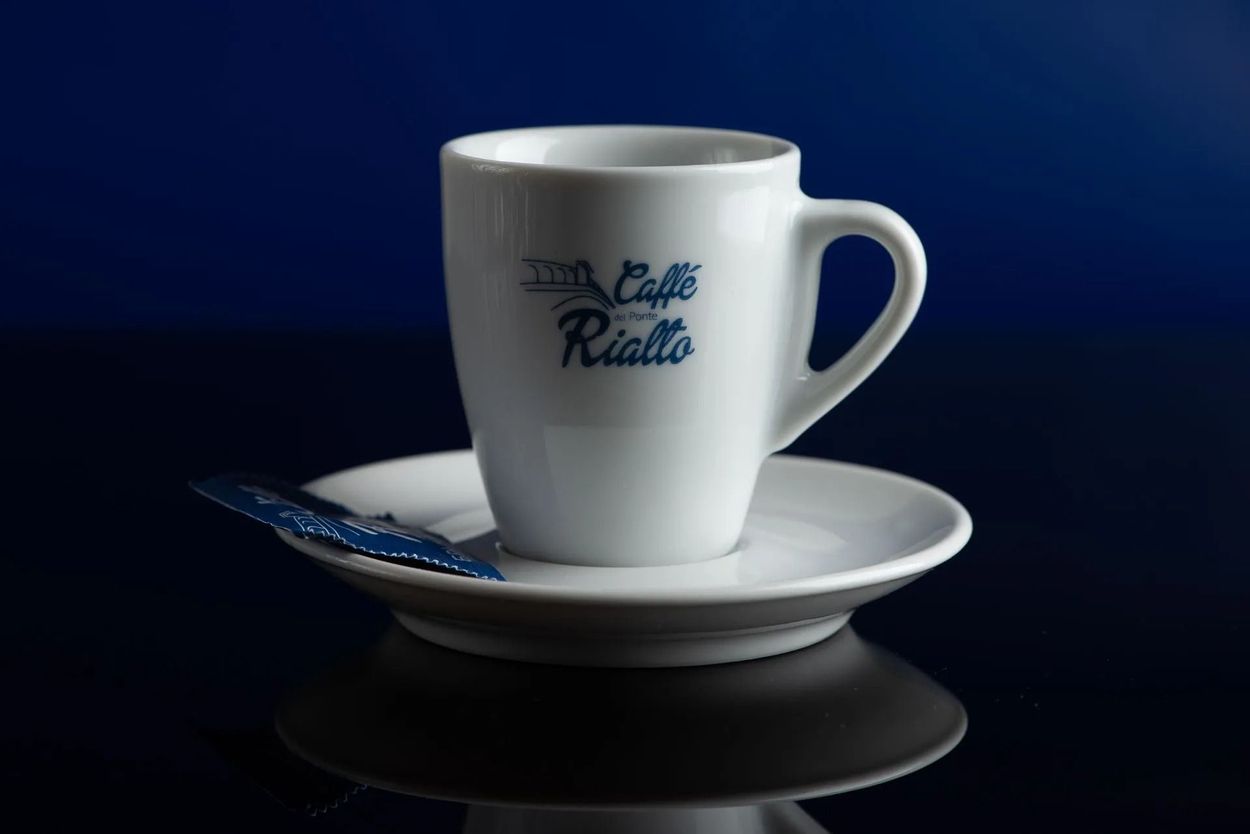 Taza de café blanca sobre platillo con cuchara azul sobre fondo azul oscuro