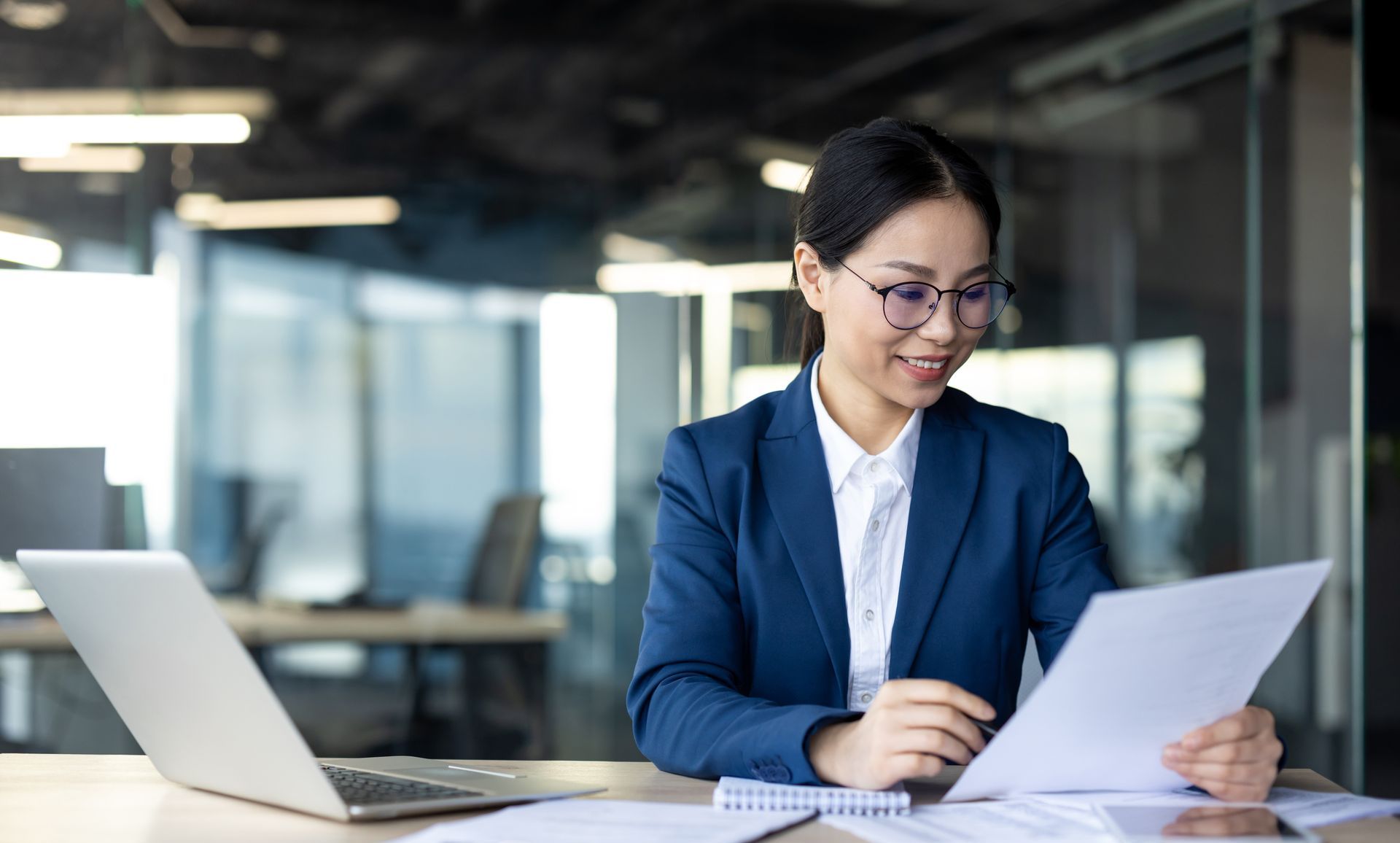 A woman is sitting at a desk with a laptop and papers.