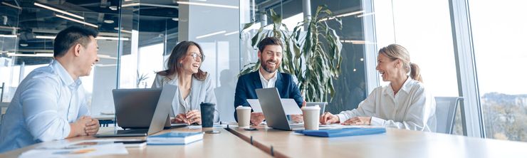 A group of people are sitting around a conference table with laptops.