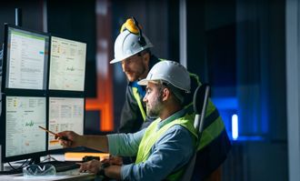 Two men in hard hats are looking at a computer screen.