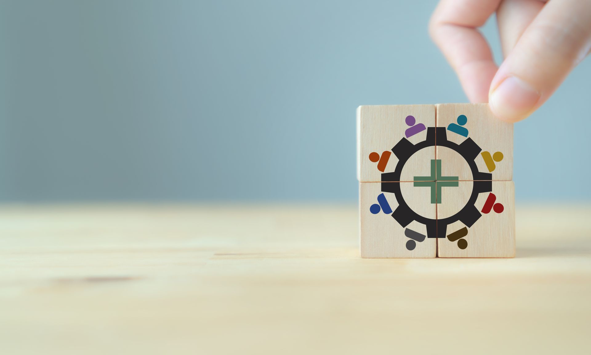 A person is holding a wooden block with a cross in the middle.