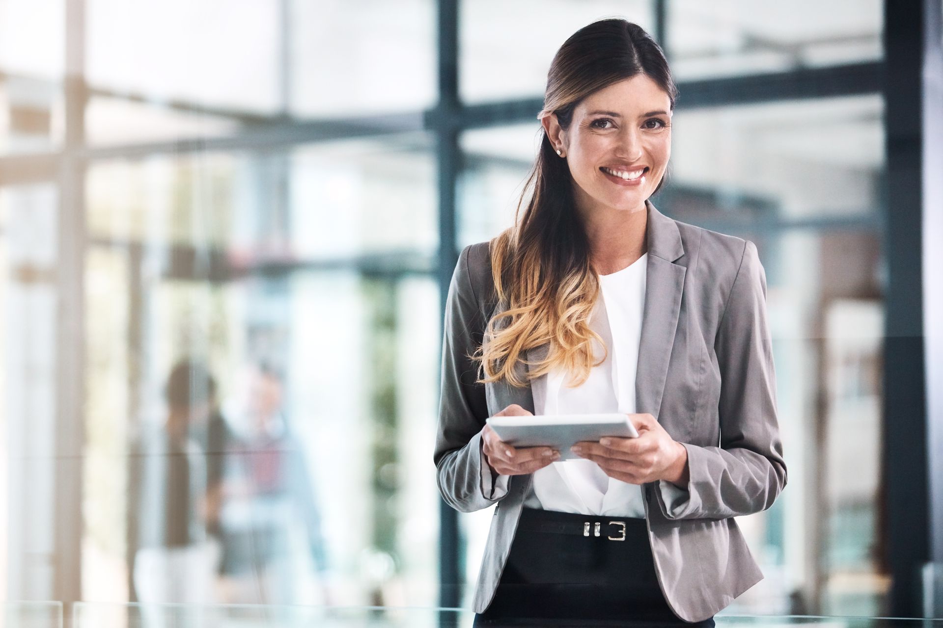 A woman in a suit is holding a tablet and smiling.