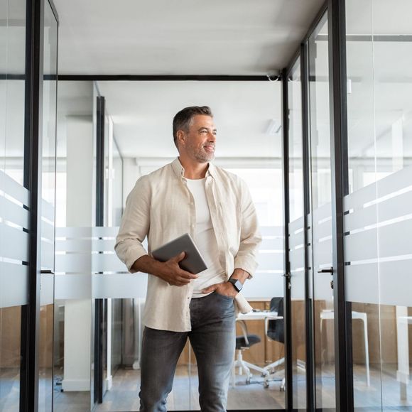 A man is walking through a glass door holding a tablet.