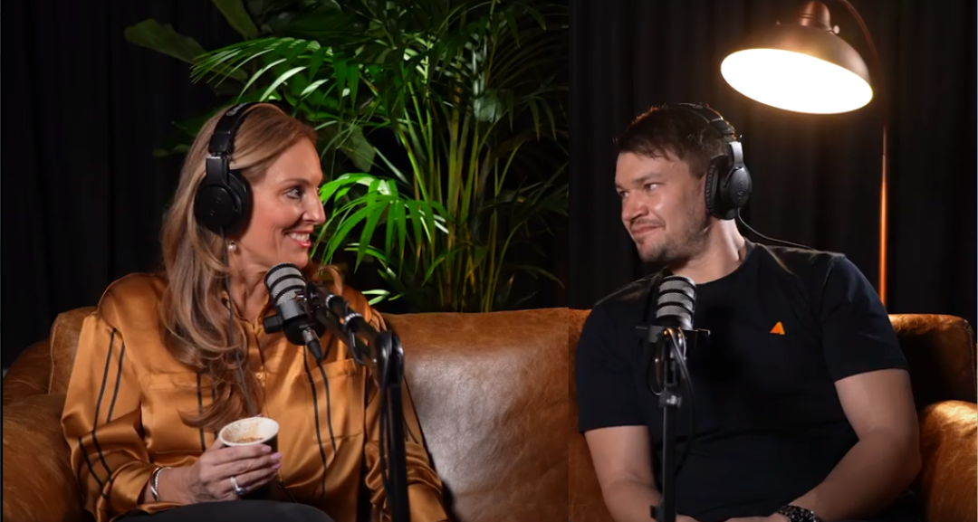 A man and a woman are sitting on a couch talking into microphones.