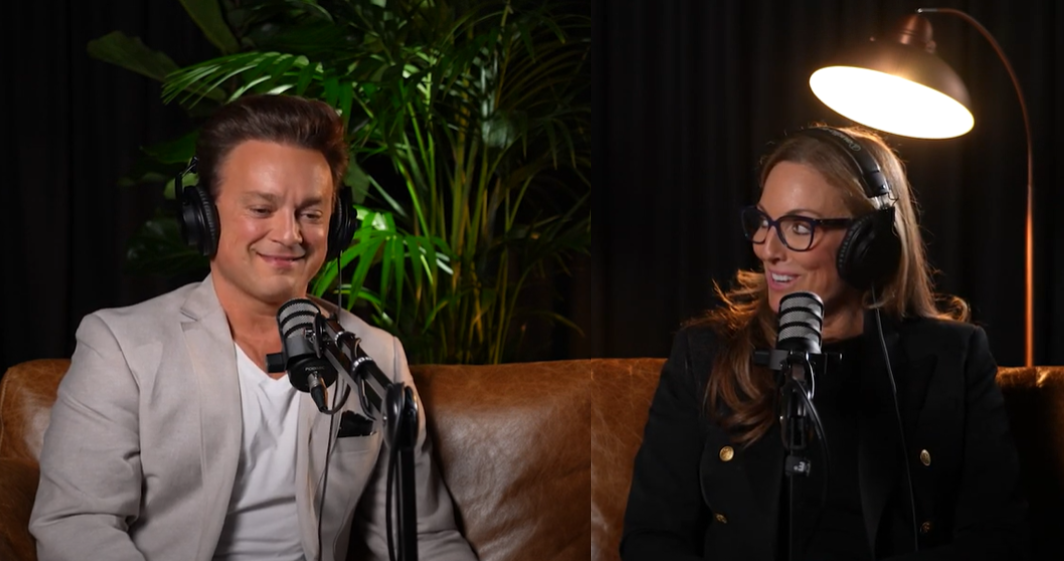 A man and a woman are sitting on a couch talking into microphones.