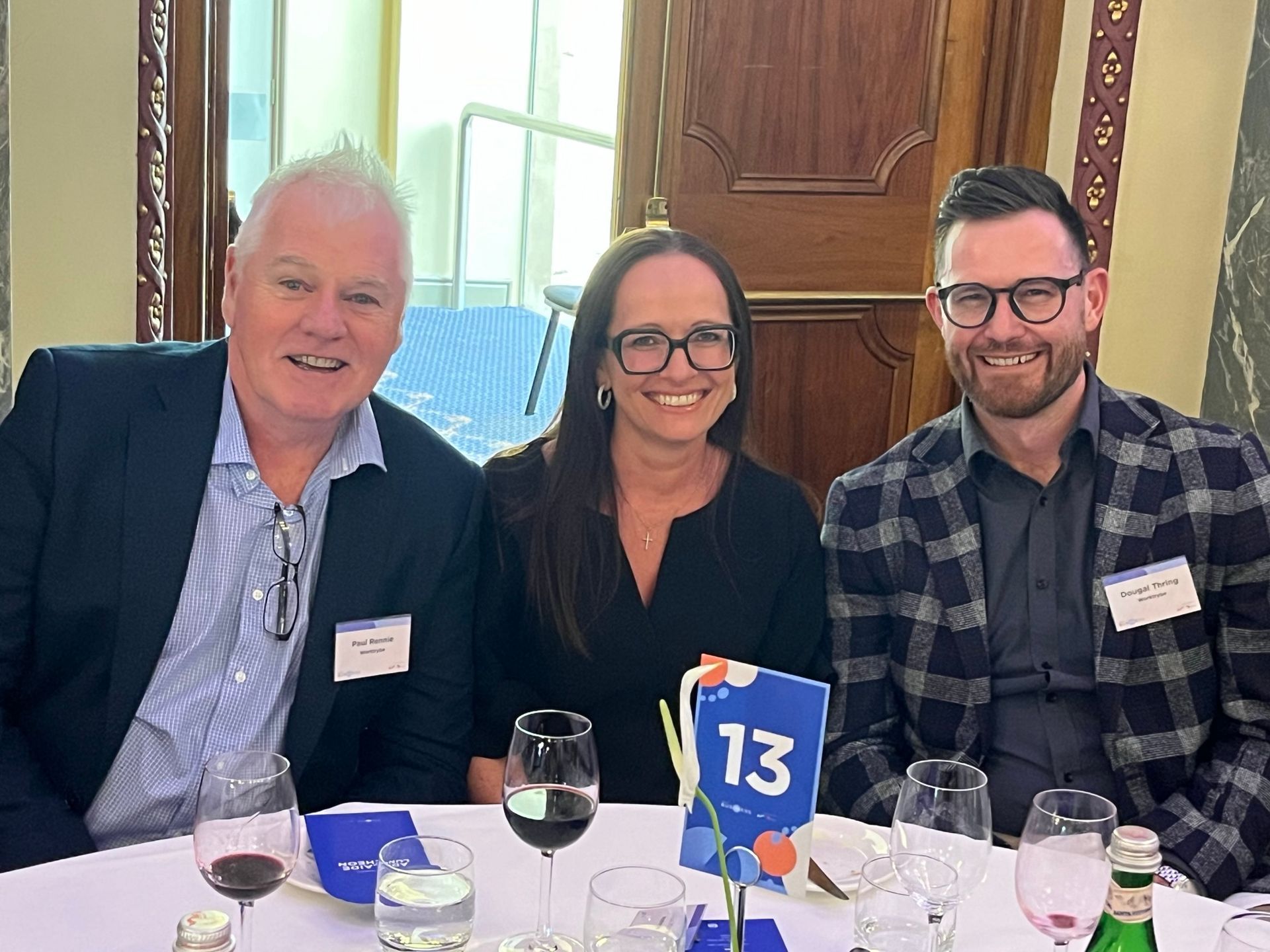 Three people are sitting at a table with wine glasses and a blue table number.