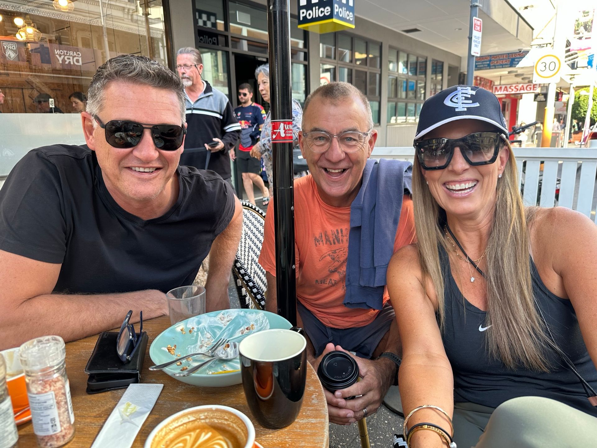 Three people are sitting at a table with a plate of food and a cup of coffee.