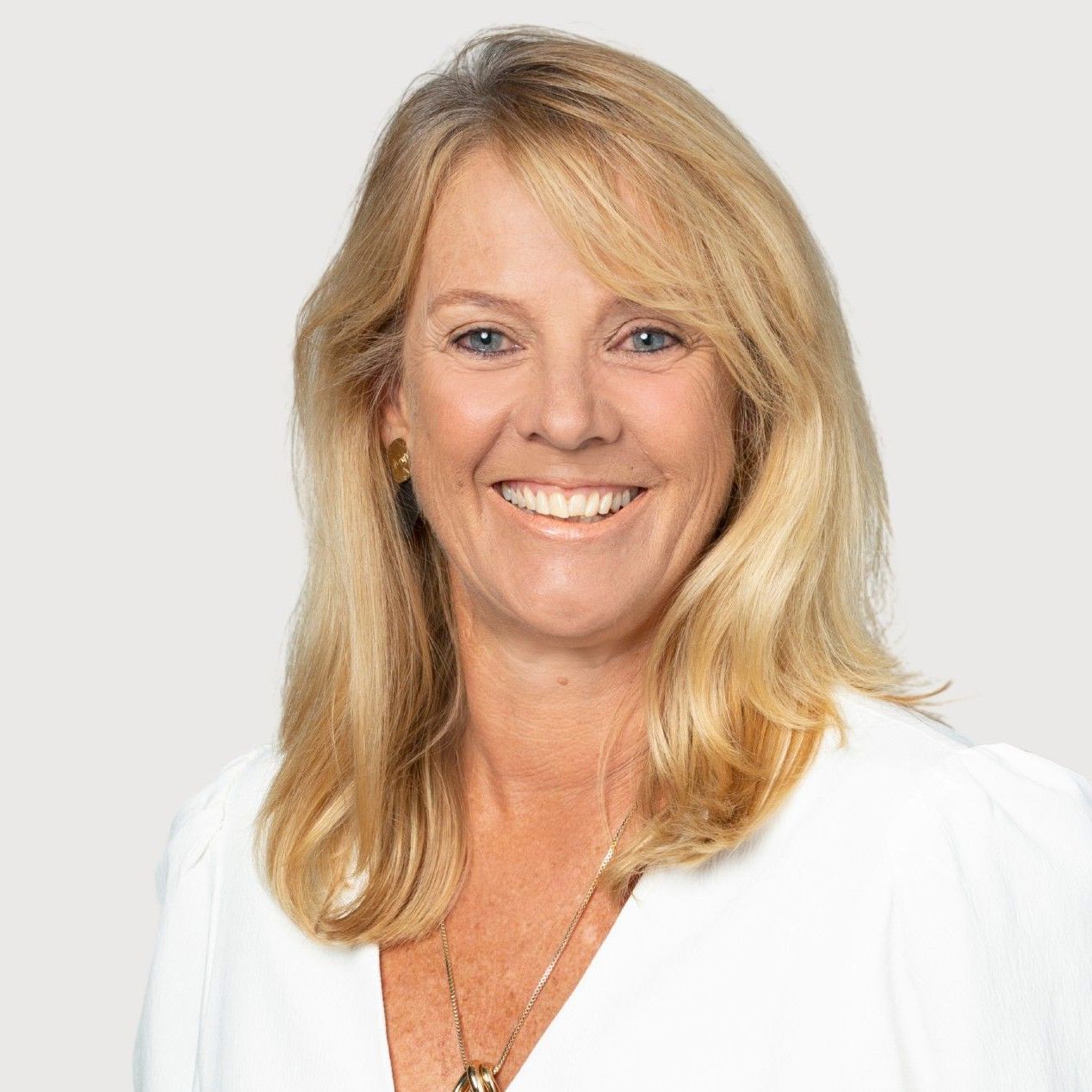 A woman wearing a white shirt and a necklace is smiling for the camera.