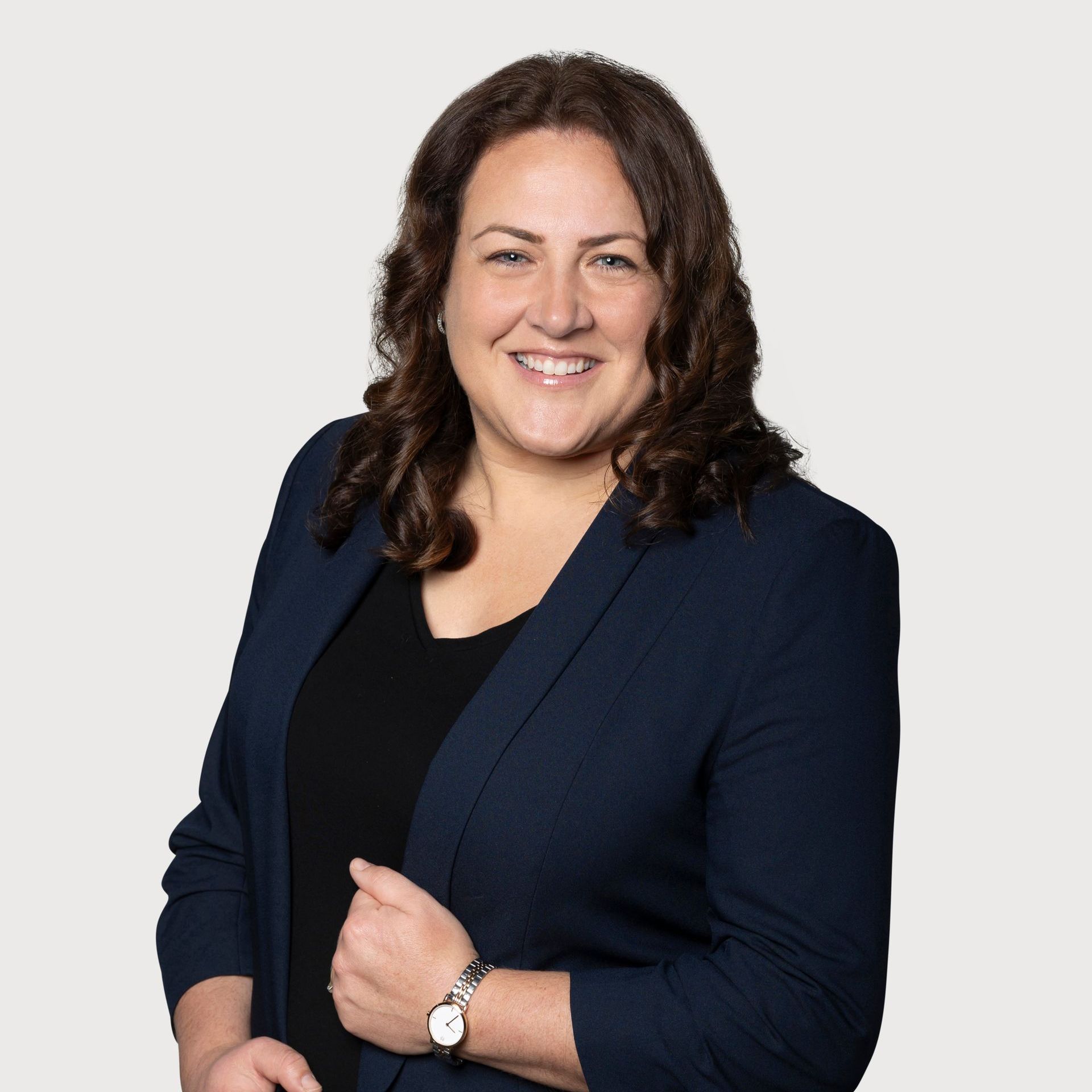 A woman wearing a black shirt and a blue jacket is smiling for the camera.