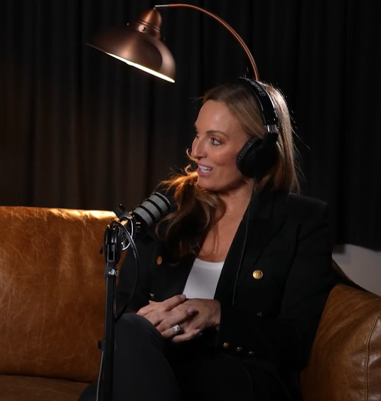 A woman wearing headphones is sitting on a couch in front of a microphone