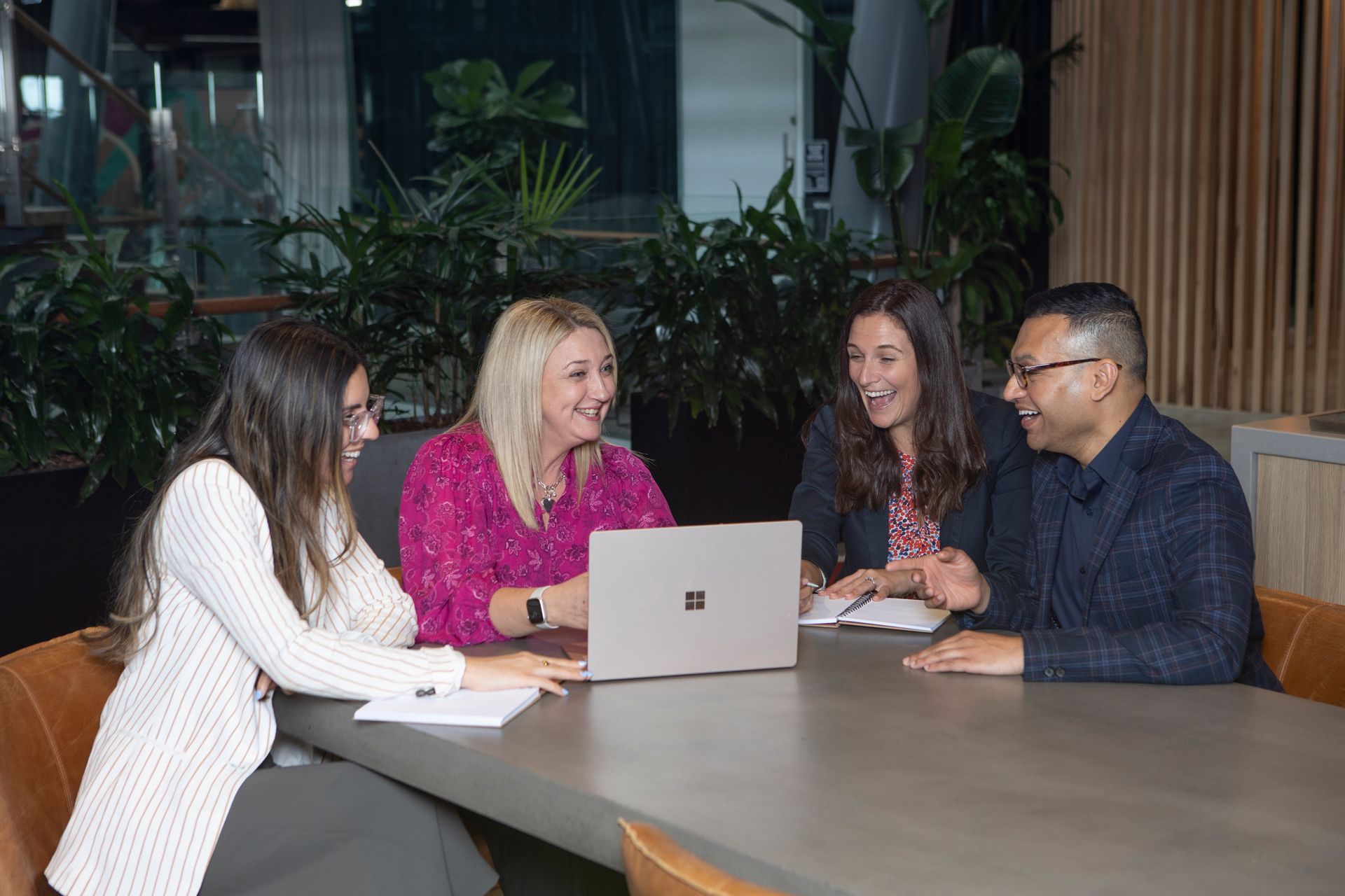 A group of people are sitting around a table looking at a laptop.