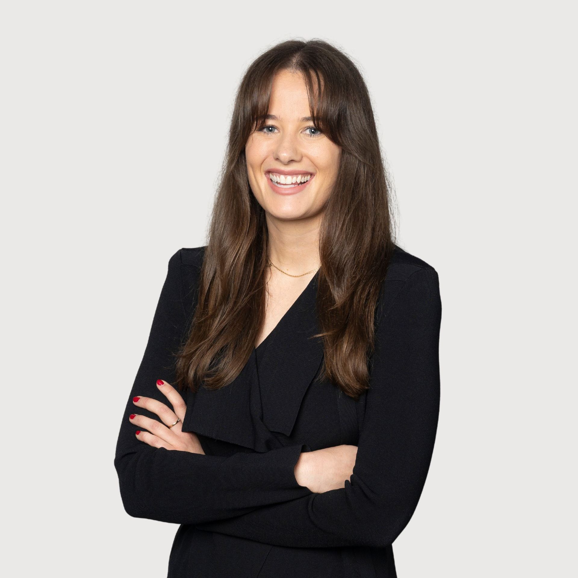 A woman in a grey jacket is smiling with her arms crossed