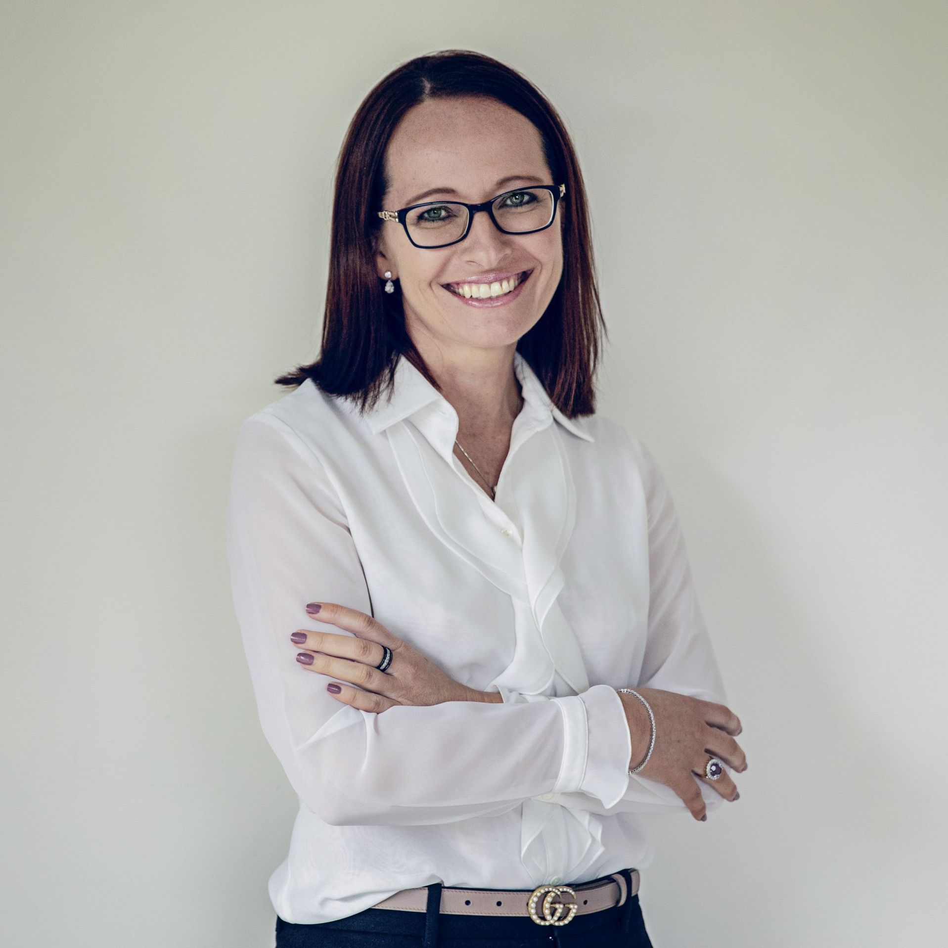 A woman wearing glasses and a white shirt is smiling with her arms crossed.