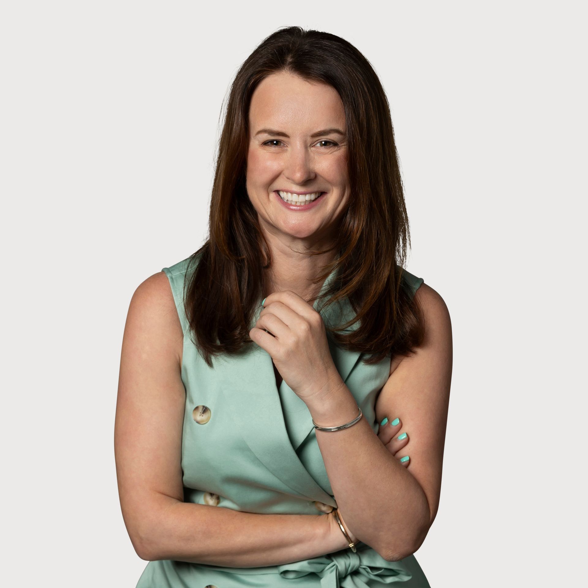 A woman in a green dress is smiling with her arms crossed.