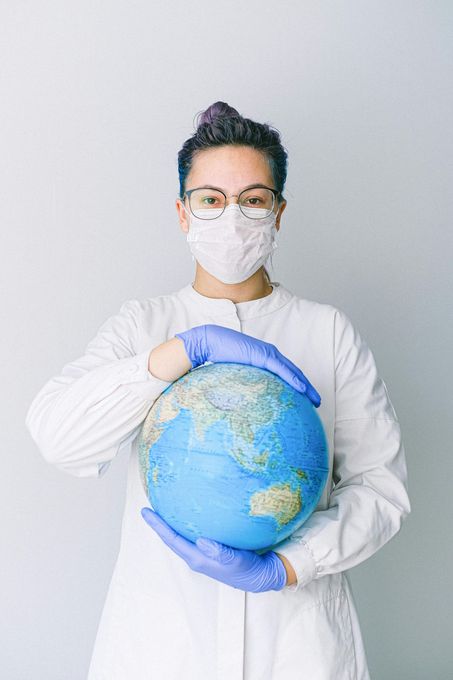A woman wearing a mask and gloves is holding a globe in her hands.