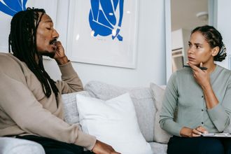 A man and a woman are sitting on a couch talking to each other.