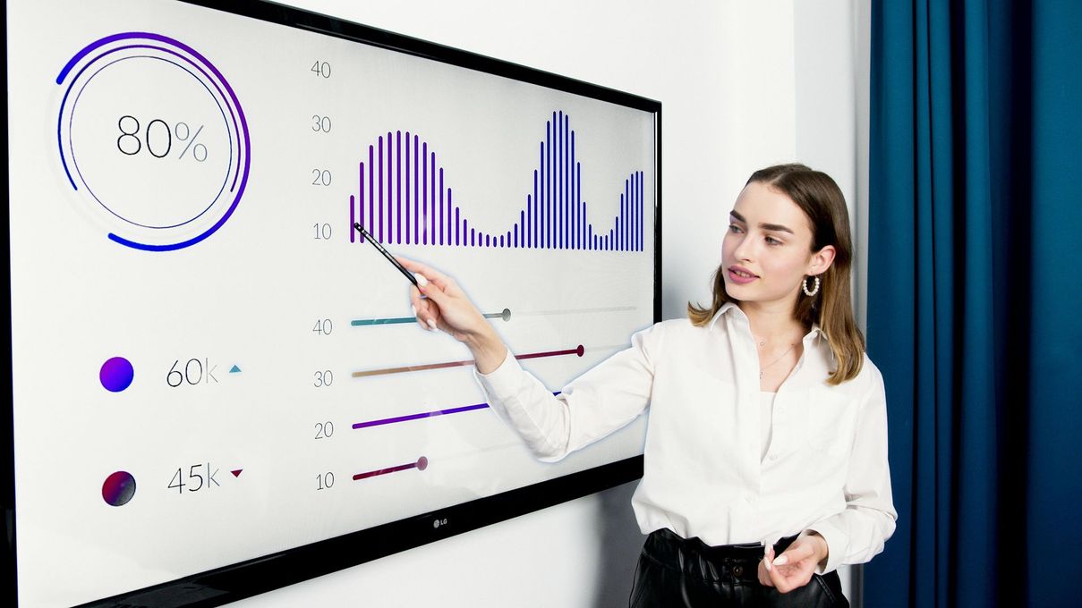 A woman is pointing at a graph on a large screen.
