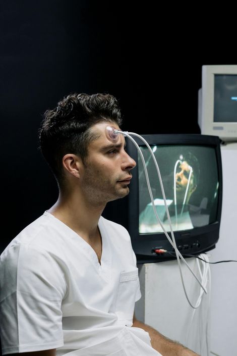A man in a white scrub is sitting in front of a television.