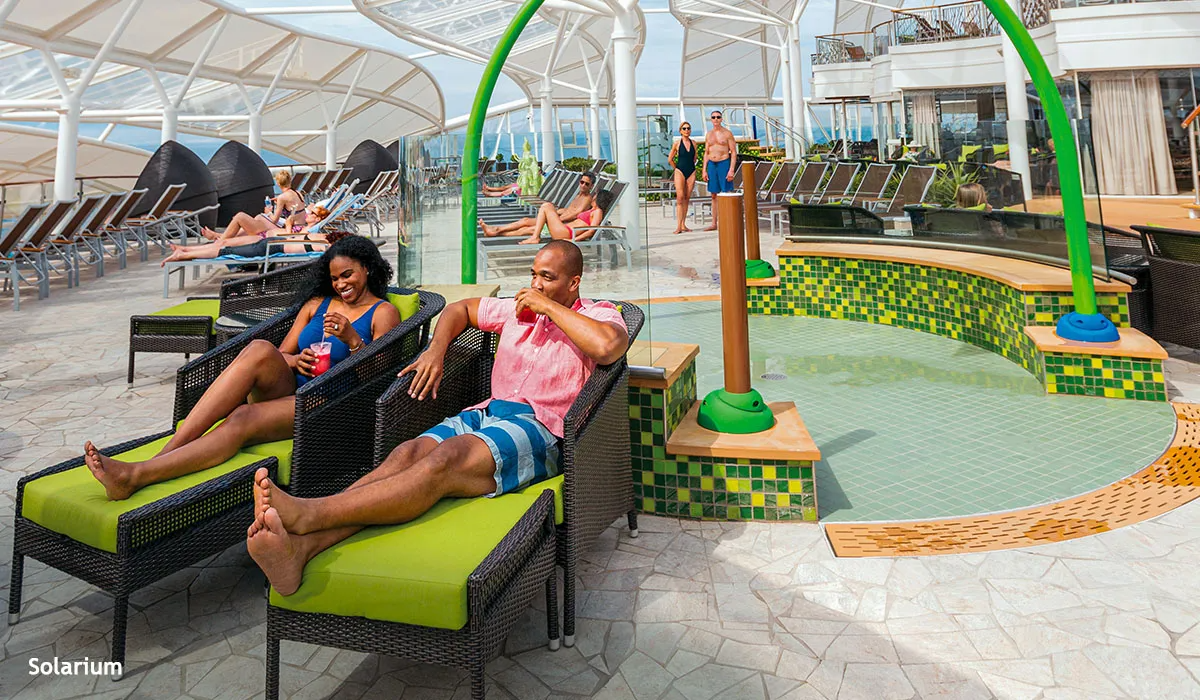 Couple relaxes on lounge chairs near a pool on a cruise ship deck.
