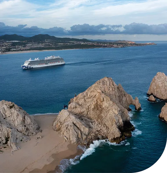 Ocean view of rocky cliffs and a cruise ship sailing near a coastline under a cloudy sky.
