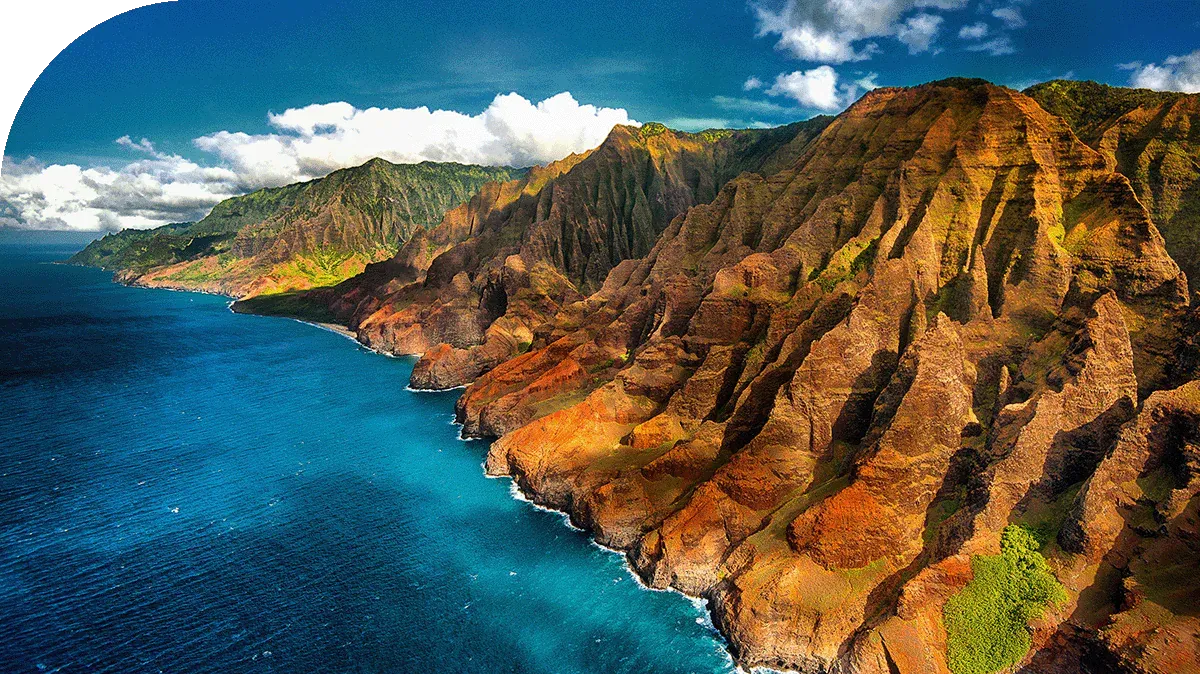 Coastal cliffs meet blue ocean under a partly cloudy sky; rugged terrain.
