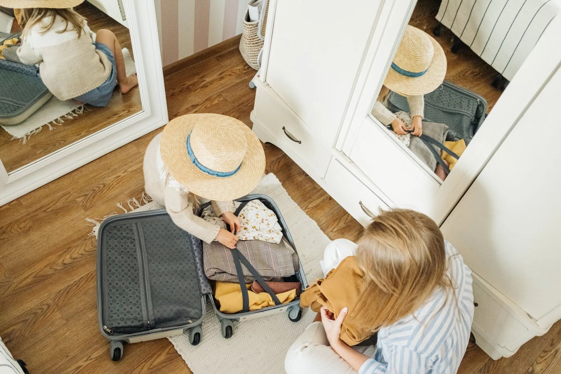Two people packing a suitcase in a bedroom, one reflected in a mirror.