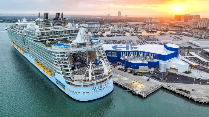 Large cruise ship docked at a port, with blue waters and a sunset in the background.