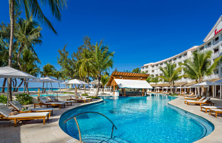 Poolside resort with blue water, palm trees, and sunny sky.